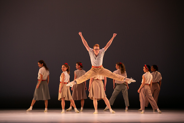 A male dancer jumps in front of a lie of female dancers