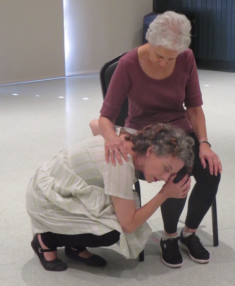 A woman in a chair comforts a woman kneeling beside her