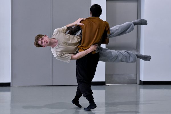 A dancer in a brown shirt lifts another dancer